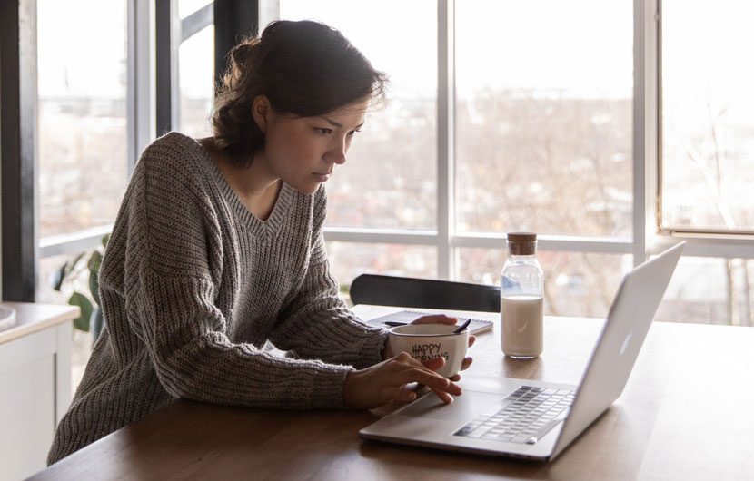 Mulher jovem acede ao computador portátil no conforto de sua casa